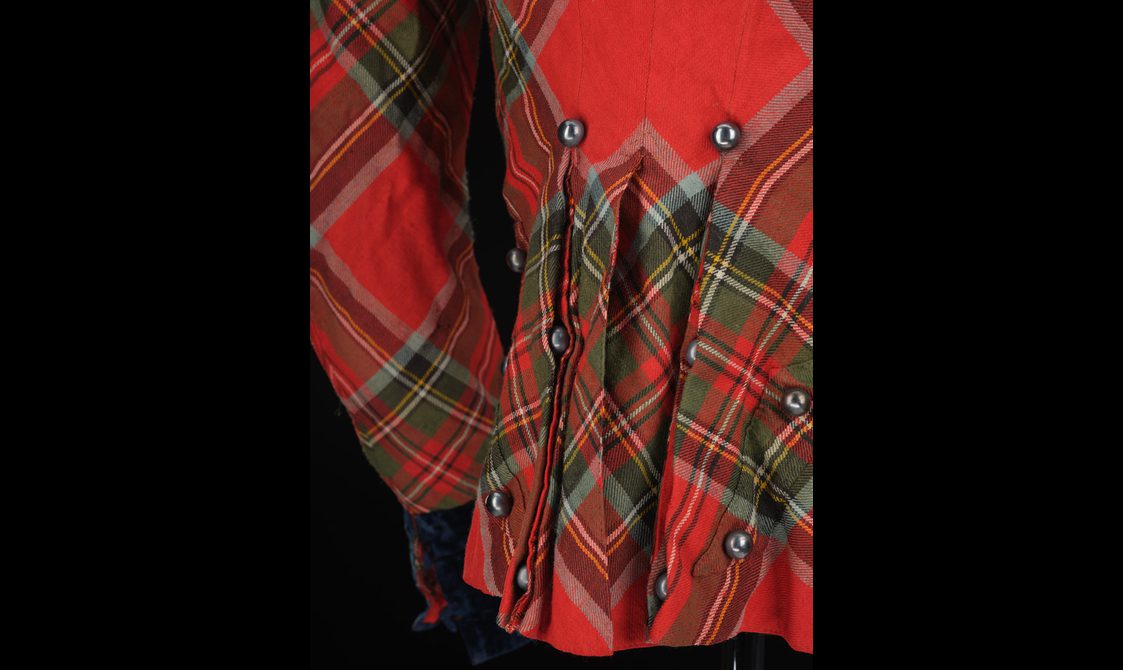 Detail of pleats and buttons on the back of a red tartan jacket.