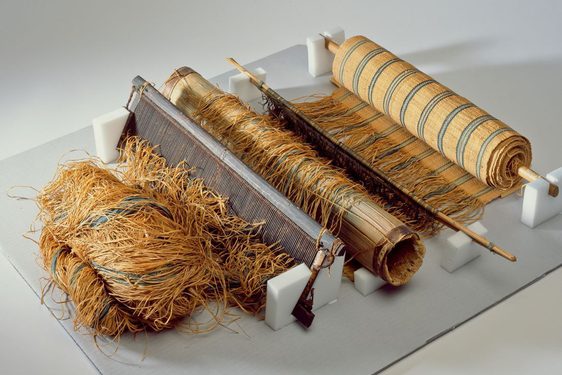 A loom with a roll of striped fabric wrapped around a spool with fibers running from it.