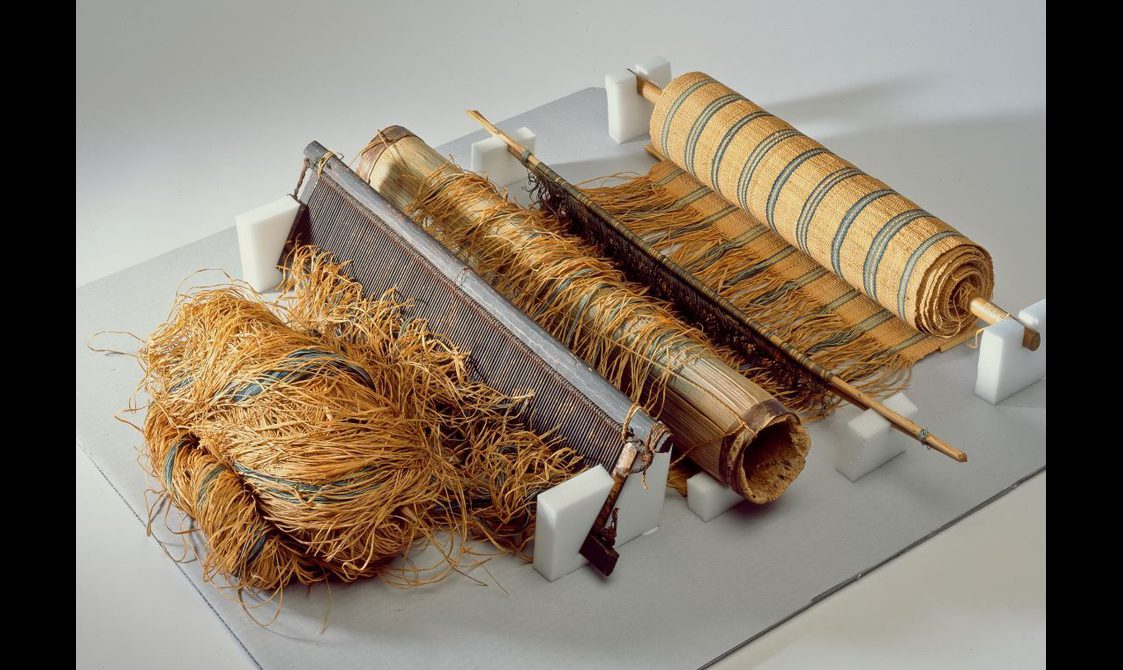 A loom with a roll of striped fabric wrapped around a spool with fibers running from it.