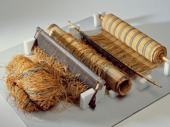 A loom with a roll of striped fabric wrapped around a spool with fibers running from it.