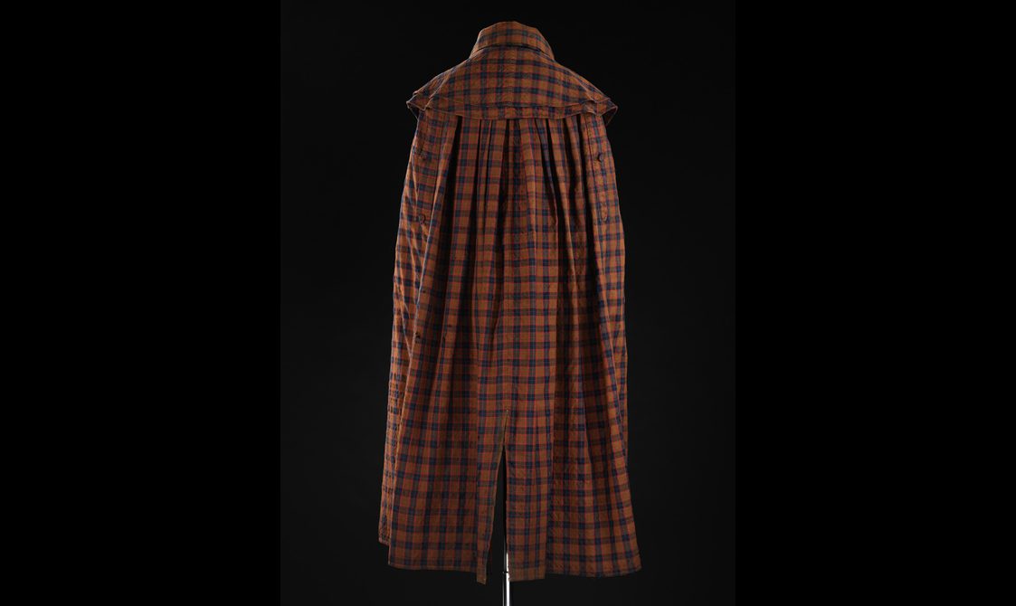Back view of a mannequin wearing a long brown, navy, and red tartan cloak