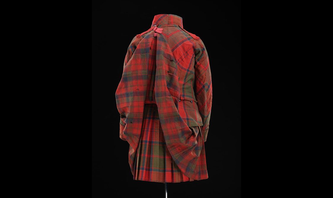 Back view of a mannequin wearing a red tartan kilt with a matching jacket and pinned up tails.
