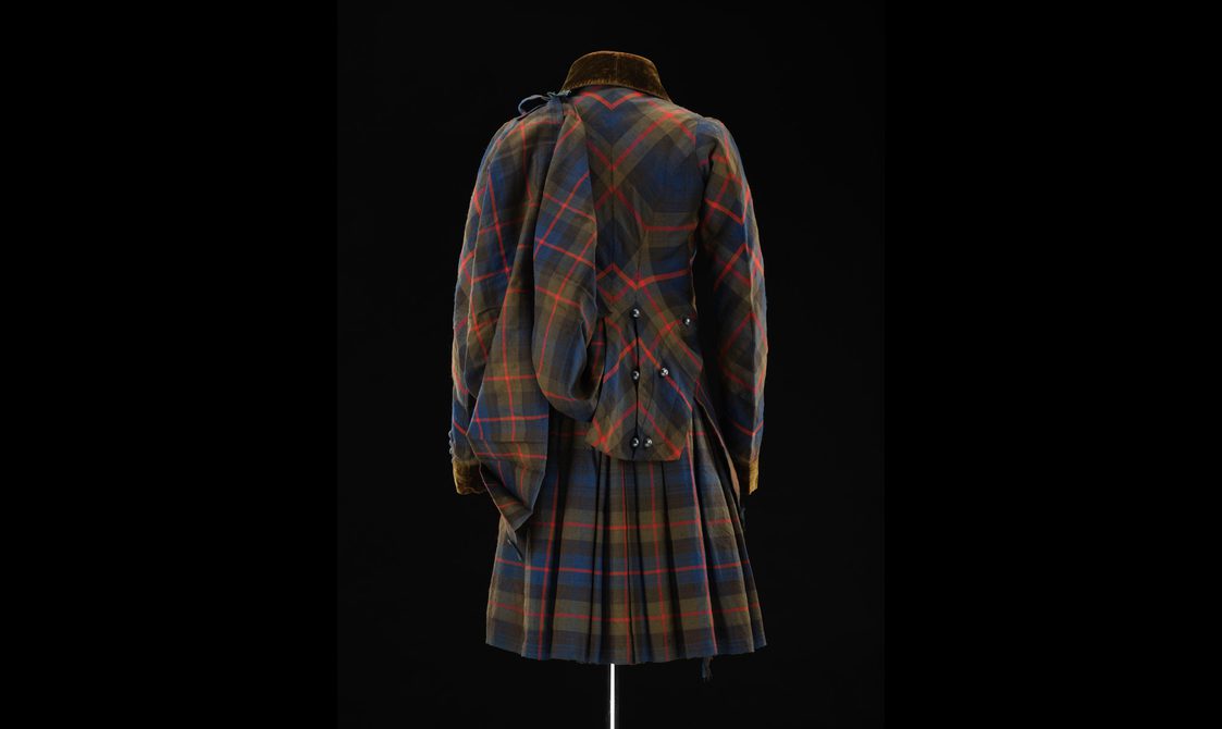 Back view of a mannequin wearing a navy, green, and red tartan kilt and matching jacket with pinned up coat tails.