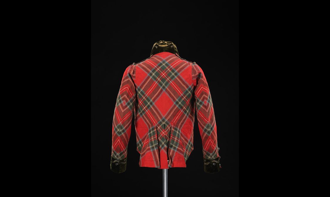 Back view of a mannequin wearing a short red tartan jacket with a velvet collar and cut glass buttons.