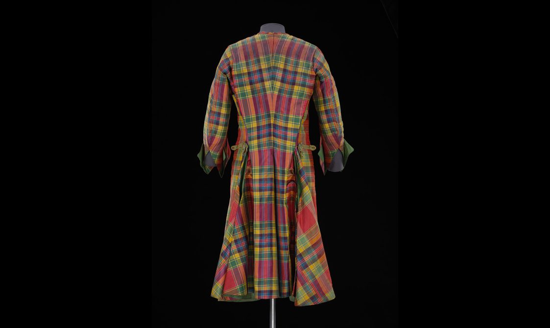 A back view of a mannequin wearing a long red, green, and yellow tartan silk jacket