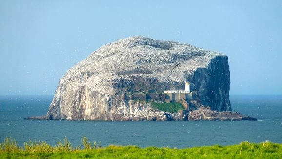 A view of an island comprised of a large rock with a building and tall walls nestled in its cliffside.