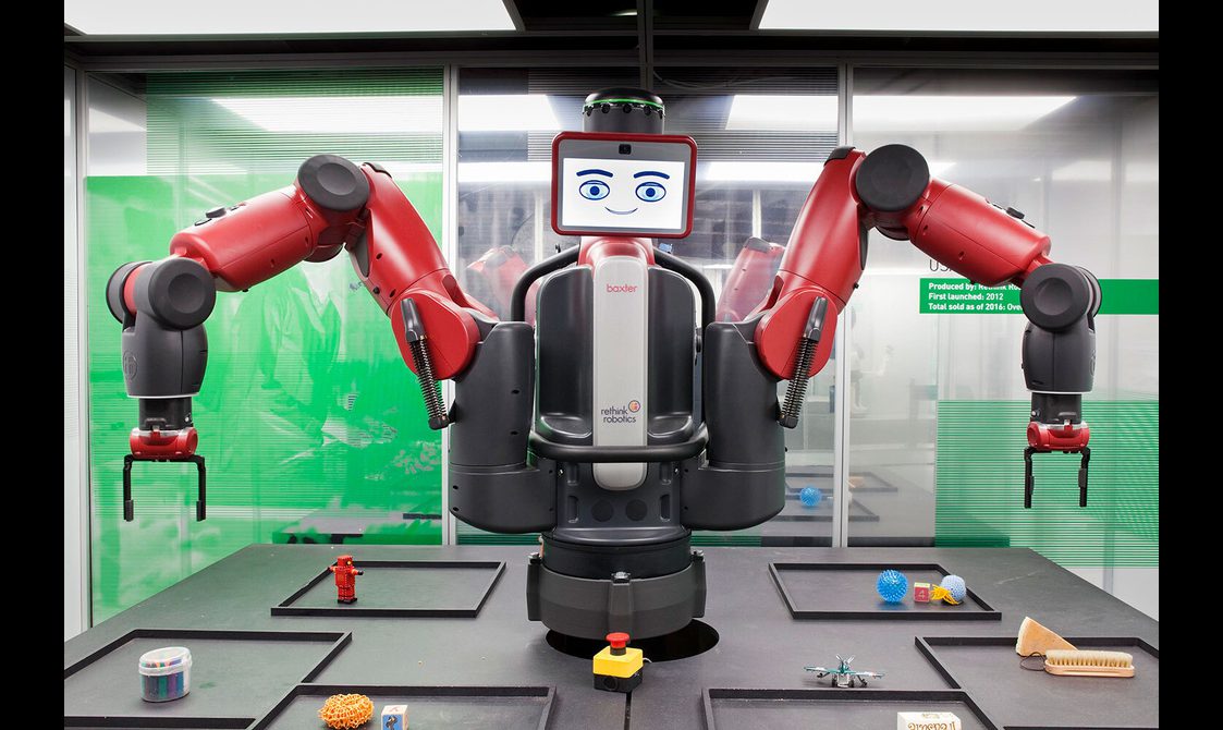 A robot with its arms raised, surrounded by objects that it can picj up.