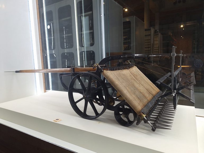 A small model of a reaping machine, on display in a small case in the museum.