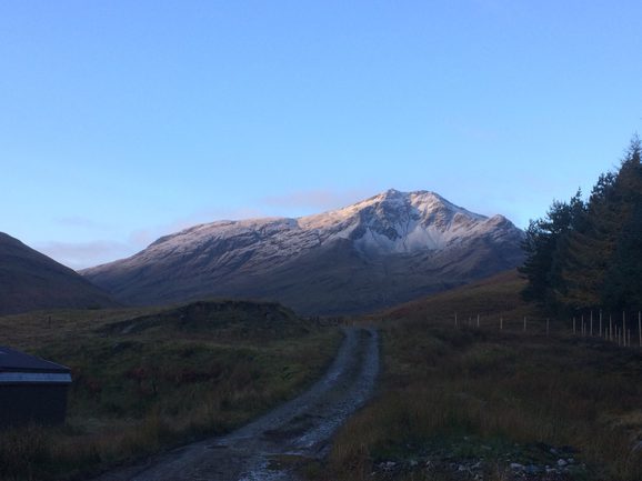 A prominent, snow-capped mountain against a blue sky with a small road leading towards it in the foreground.