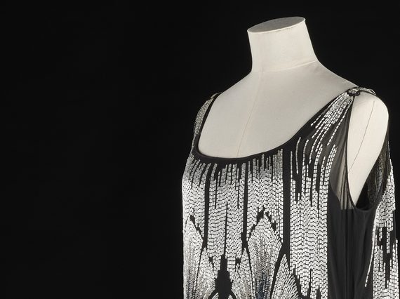 A white mannequin from the waist up wearing a black dress with silver beading in an art deco style