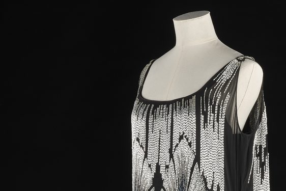 A white mannequin from the waist up wearing a black dress with silver beading in an art deco style