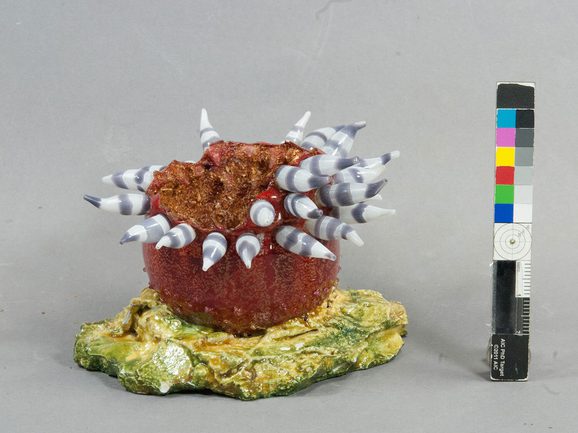 A side view of a broken model of a sea anemone, made of grey and red coloured glass