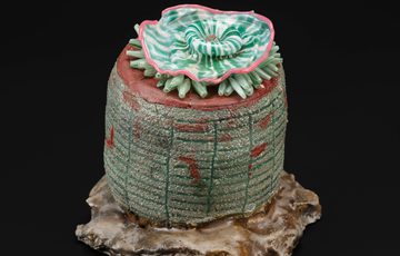 A colourful glass sculpture of a brown rock with a mottled green pillar and a green and pink jellyfish like sea-creature on top