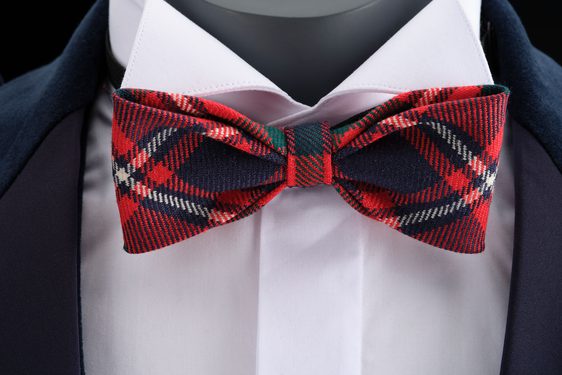 A close up of a mannequin wearing a white shirt, navy jacket, and a red tartan bowtie