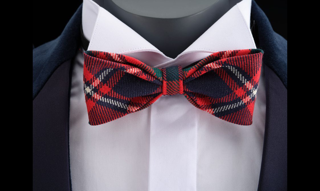 A close up of a mannequin wearing a white shirt, navy jacket, and a red tartan bowtie