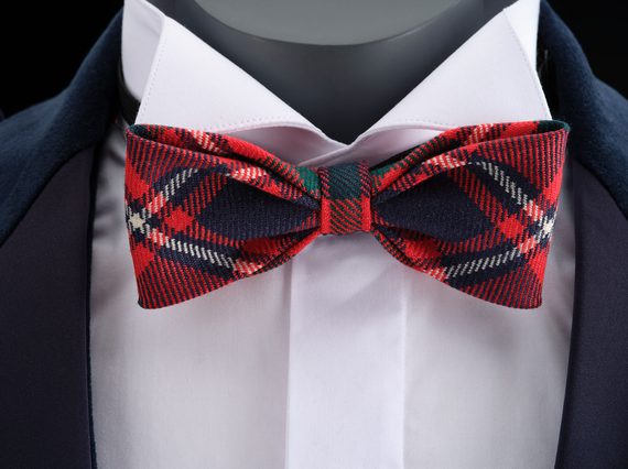 A close up of a mannequin wearing a white shirt, navy jacket, and a red tartan bowtie