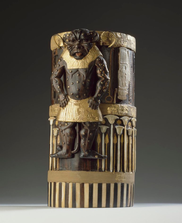 A cylindrical box made of wood, gold, and ivory with decorative elements including a lion-like figure.