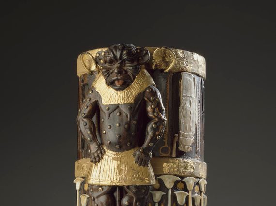 A cylindrical box made of wood, gold, and ivory with decorative elements including a lion-like figure.