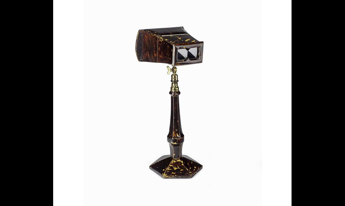 A binocular type of object made of brown tortoise shell on a gold and tortoise shell stand.