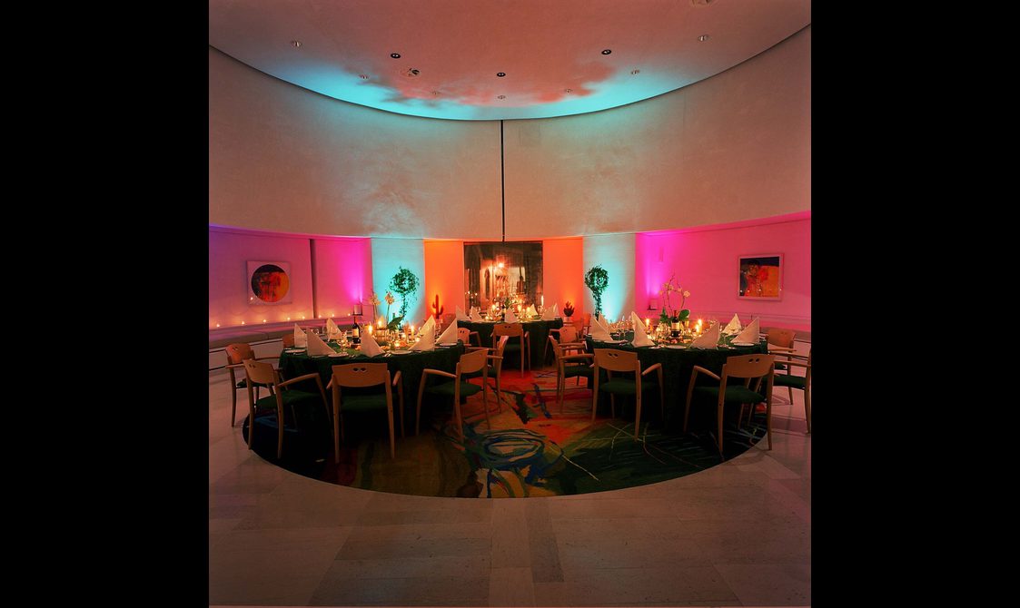 Tables set up for dinner in a circular room with multi-coloured lights on the walls.