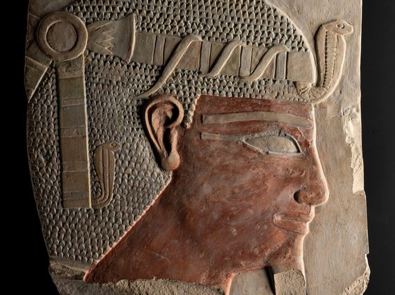 A stone carving of an Egyptian figure's head wearing a headdress viewed from the side.