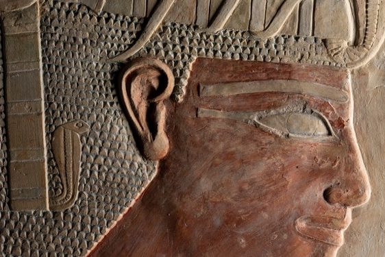 A Egyptian sculpture made of brown stone, showing a pharaoh's head with a prominent headdress and serpent motif.