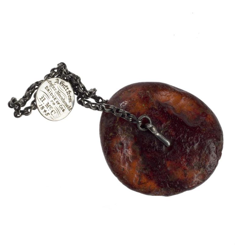 Flat circular shaped amber bead attached to a silver chain with a small medallion with an inscription.
