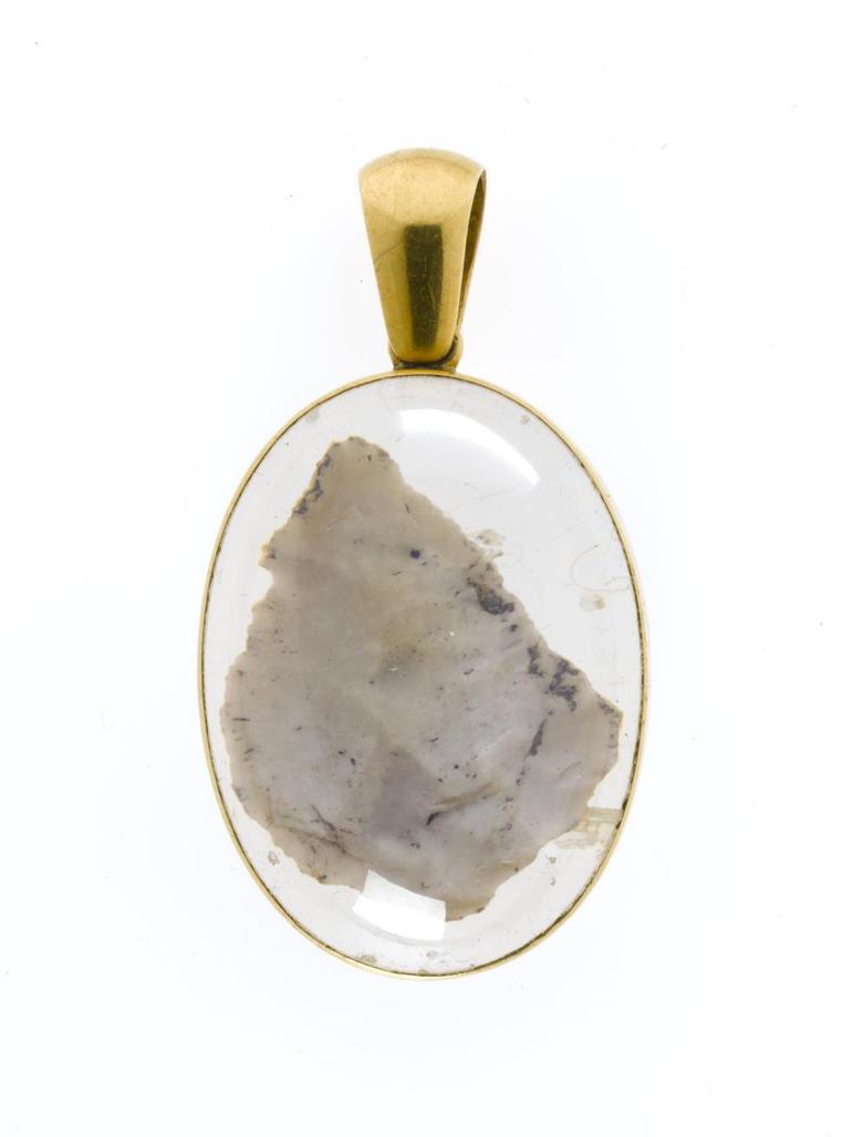 Leaf-shaped flint arrowhead set in an oval crystal container bound with gold. There is a loop for suspension.