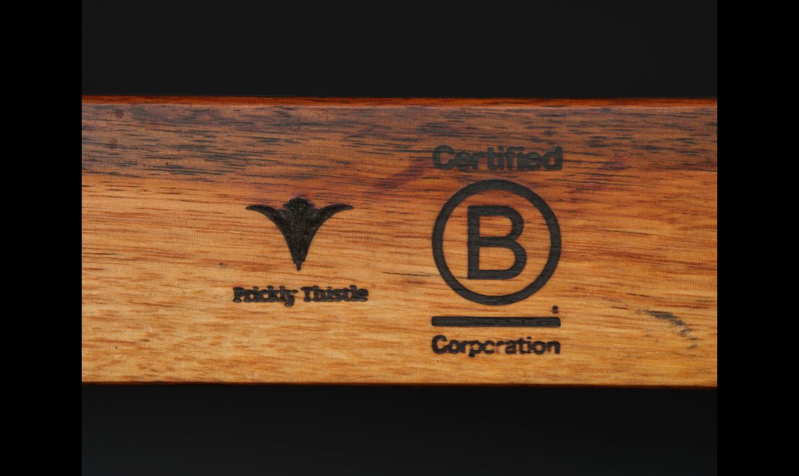 A detail of a wooden object with the company logo and a logo to denote that it is a certified B corporation.
