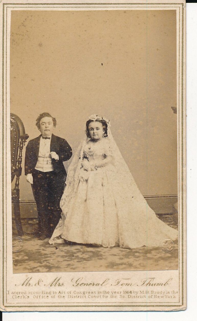 A sepia photograph of two people, who have dwarfism, in their wedding outfits.