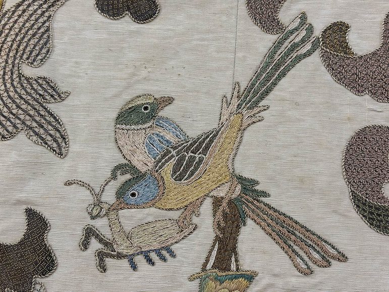 An embroidered grey cloth with two small birds eating an insect.