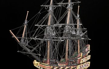 A ship model on a gold stand against a black background