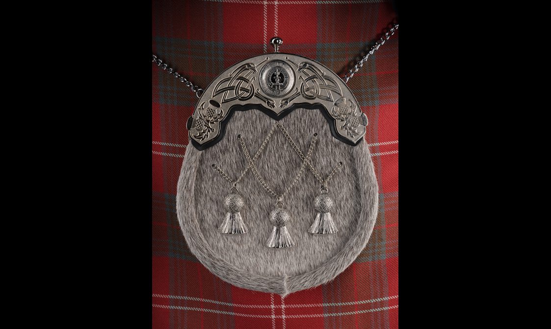 A sporran with a fur textured surface and thistle decoration, attached to a red tartan kilt.