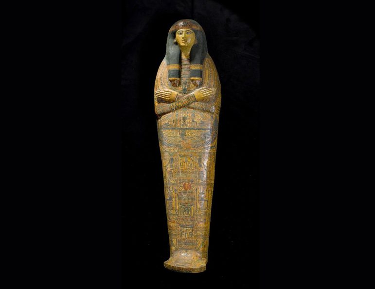 An ancient Egyptian coffin in the shape of a human. The coffin depicts a face with arms crossed at the chest, with the surface covered with illustrations and hieroglyphs