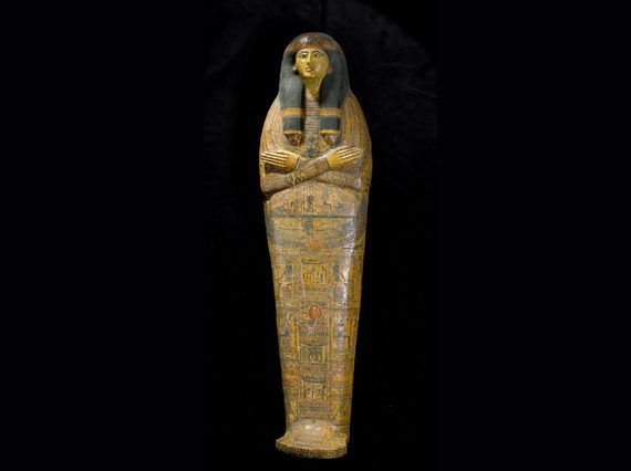 An ancient Egyptian coffin in the shape of a human. The coffin depicts a face with arms crossed at the chest, with the surface covered with illustrations and hieroglyphs
