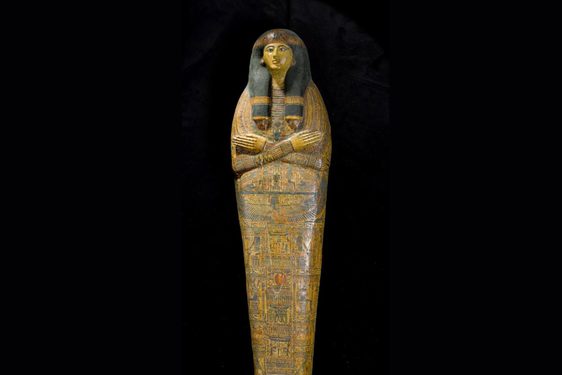 An ancient Egyptian coffin in the shape of a human. The coffin depicts a face with arms crossed at the chest, with the surface covered with illustrations and hieroglyphs