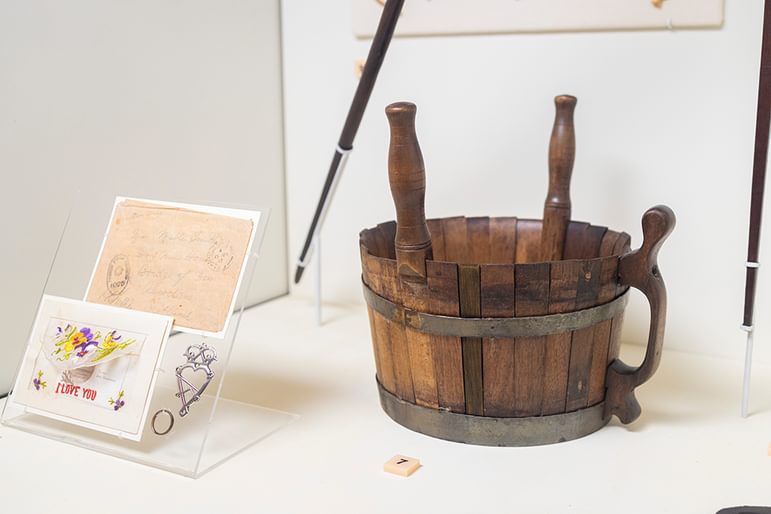 A wooden bucket or coggie with two handles on a table, surrounded by a small bicycle figurine, a lamp, and a greeting card.
