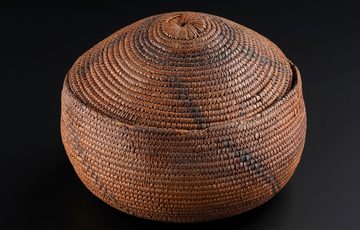 A brown round coil basket against a black background