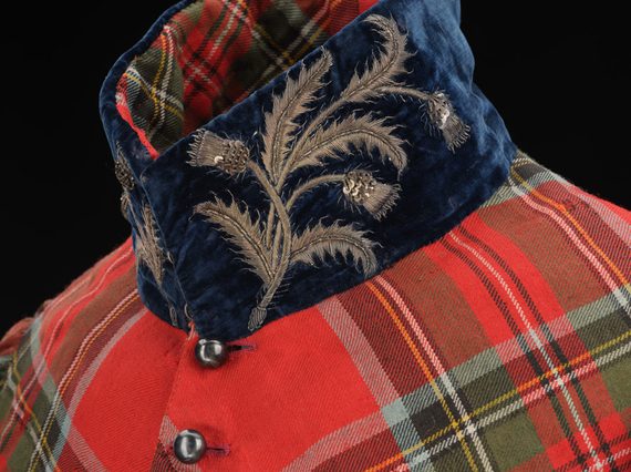Detail of a standing velvet navy collar with embroidered silver thistles on a red tartan coat.