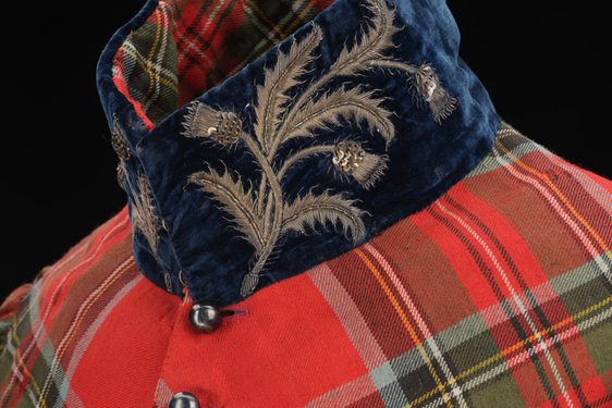 Detail of a standing velvet navy collar with embroidered silver thistles on a red tartan coat.