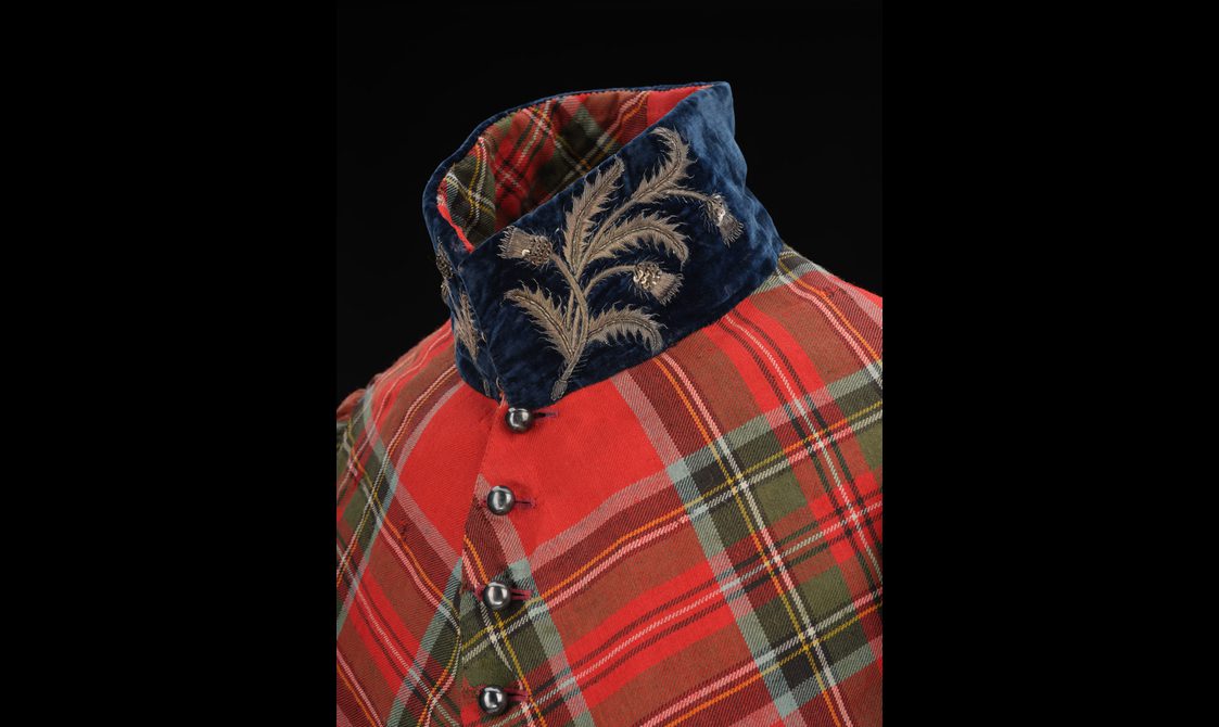 Detail of a standing velvet navy collar with embroidered silver thistles on a red tartan coat.