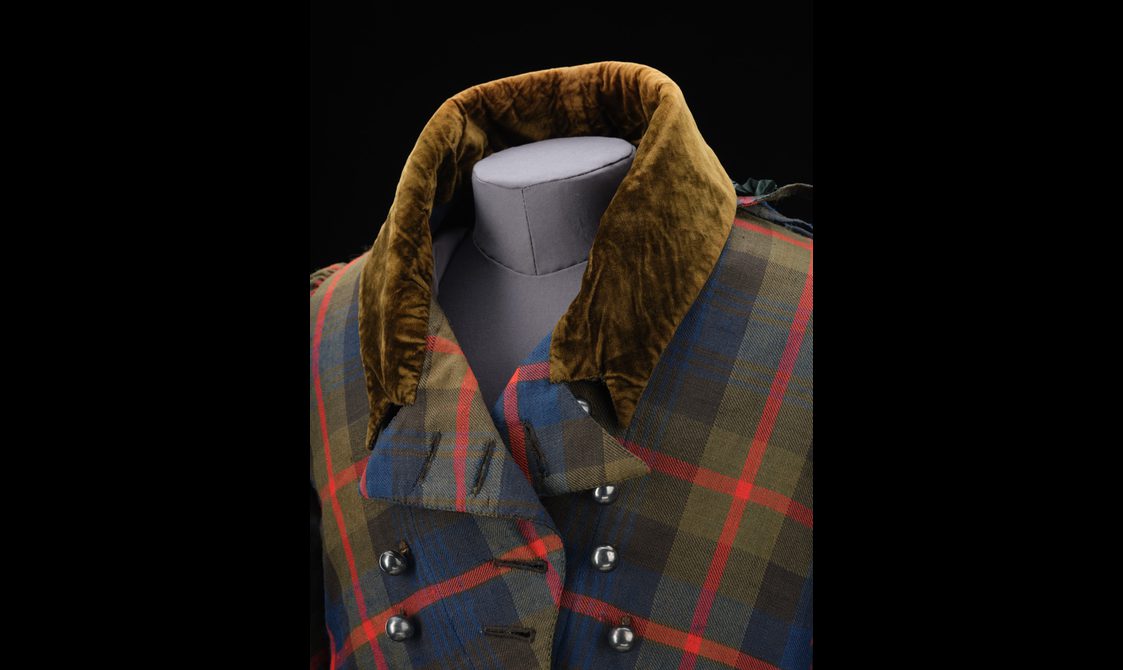 Detail of a red, navy, and green tartan jacket with an olive green velvet collar and metal buttons.