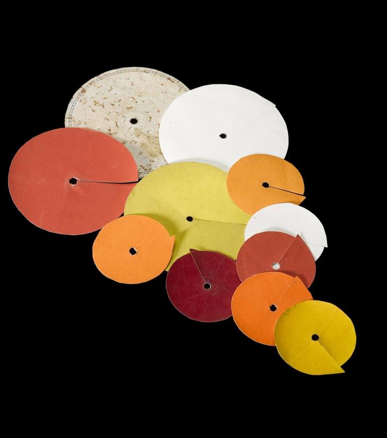 Several round pieces of white, orange, red, and yellow paper with small holes in their middles.