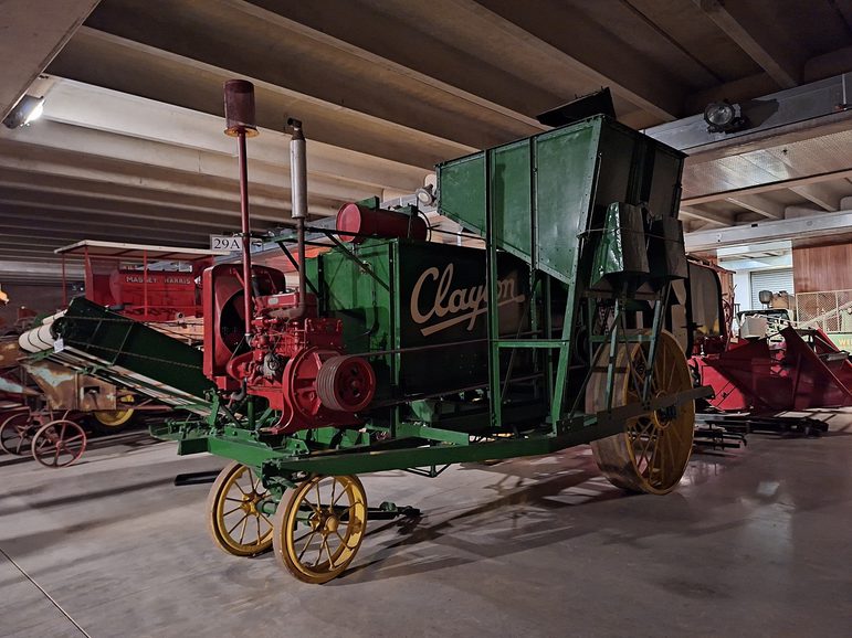 A large combine harvester in the museum store. It has a green body, with 'Clayton' written on the side in yellow. The wheels are also yellow, and the machinery at the front of it is red.