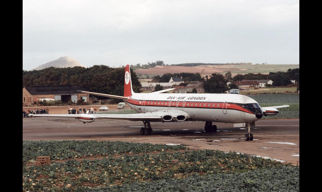 A white airplane with an orange stripe parked on a runway.