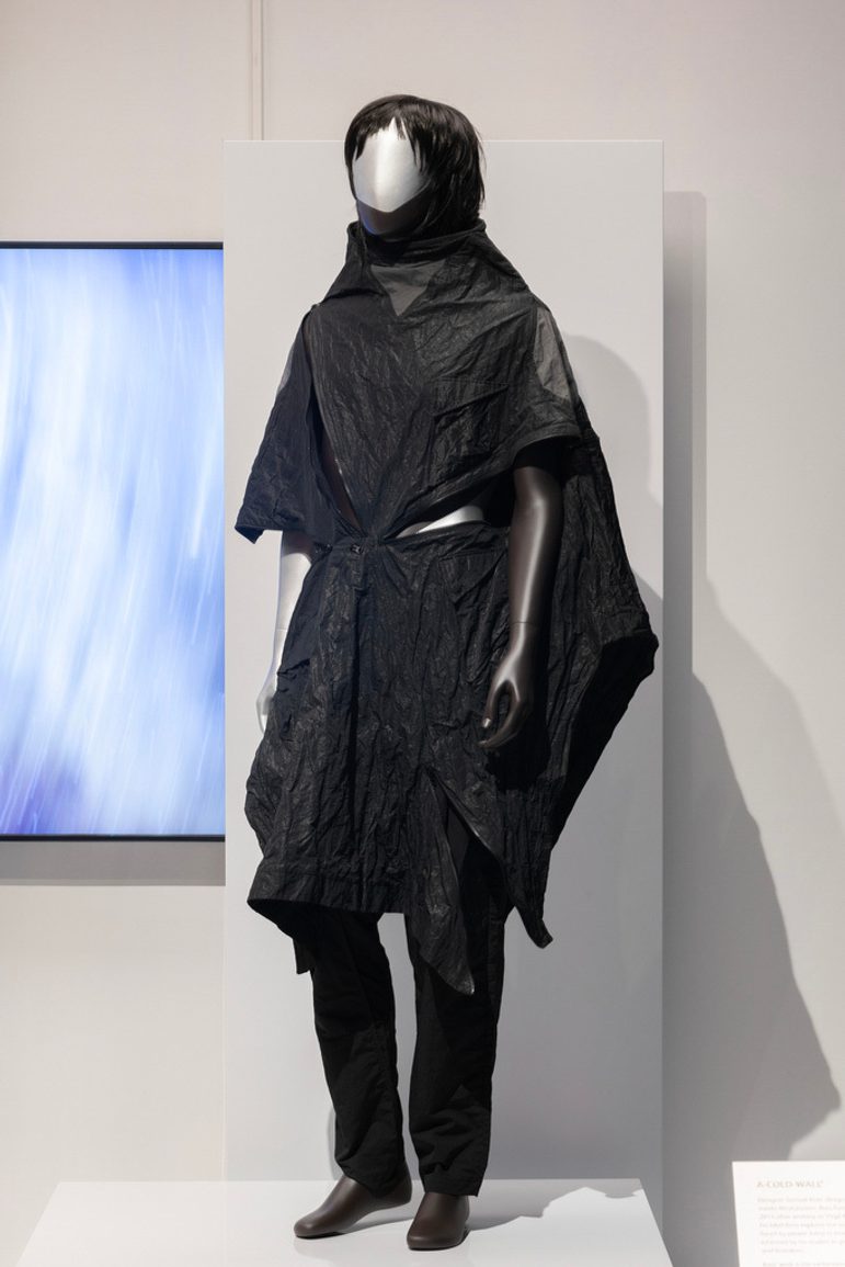 A mannequin wearing a black poncho and black trousers with a short black haired wig