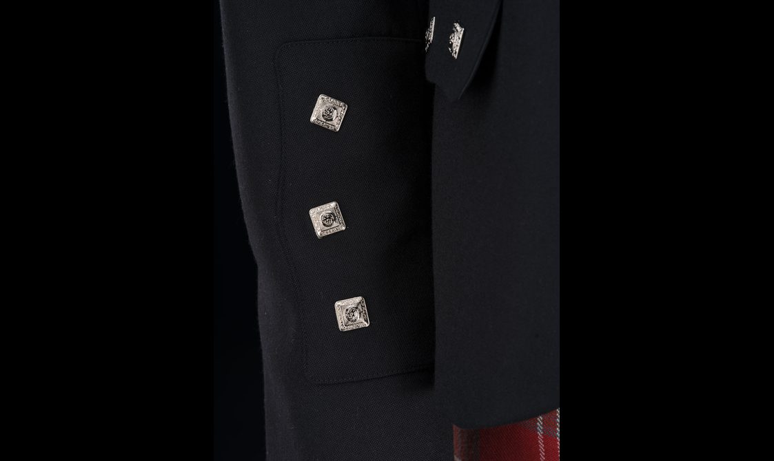 A detail of a sleeve of a black jacket with three silver square buttons on the cuff.