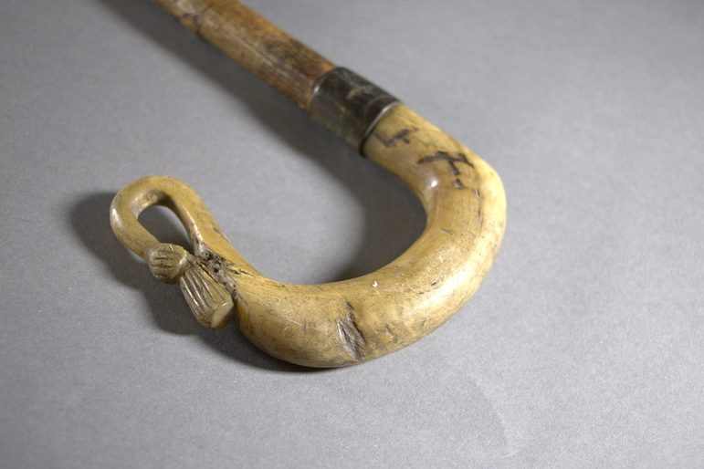 The curved end of a shepherd's crook, showing a thistle emblem at the very end.
