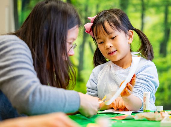 A parent and child sitting at a table doing a crafts activity.