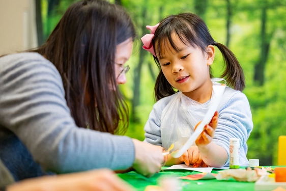 A parent and child sitting at a table doing a crafts activity.